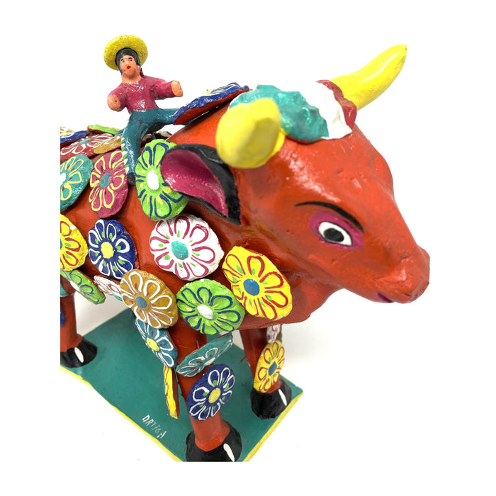 A colorful ceramic figurine of a bull with a human rider, adorned with handcrafted flowers.