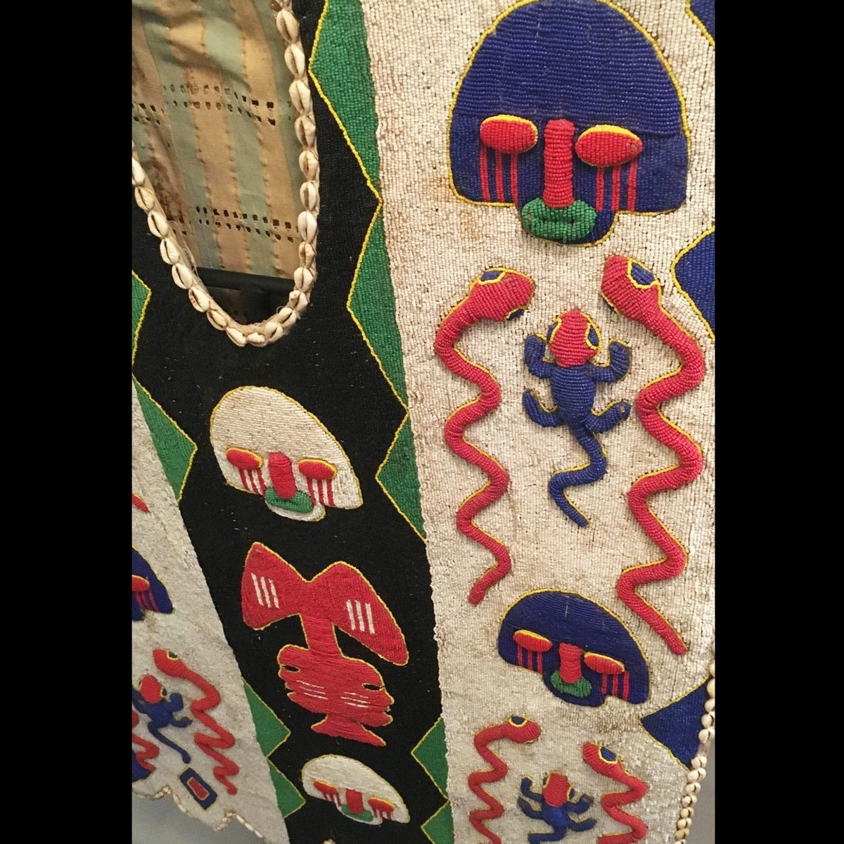 1950s Yoruba ceremonial beaded tunic with animal motifs and abstract patterns, displayed on a metal stand.