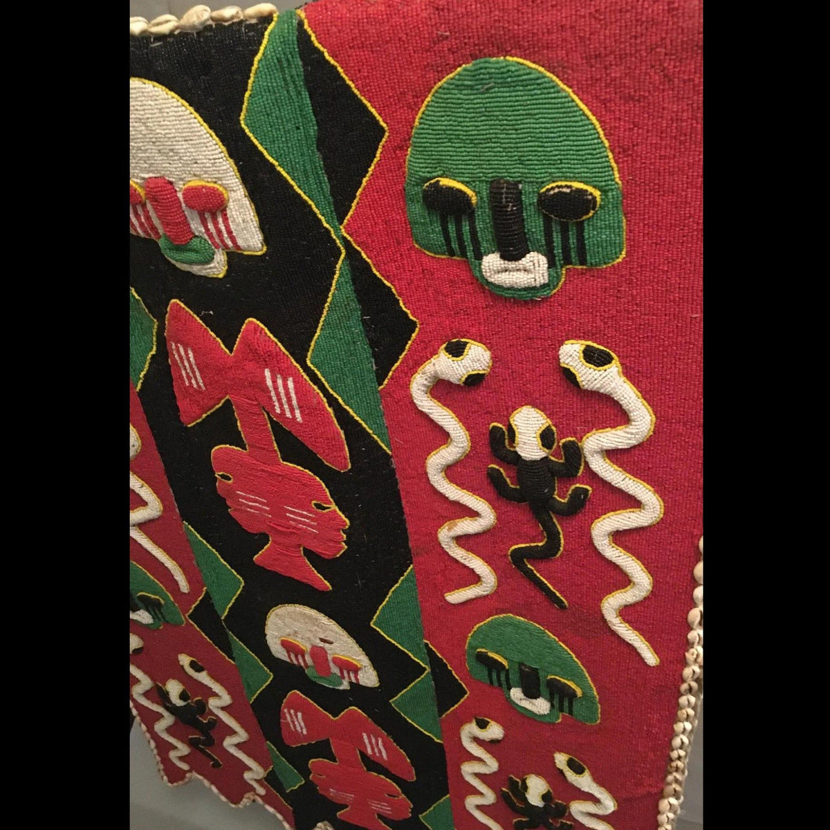 1950s Yoruba ceremonial beaded tunic with animal motifs and abstract patterns, displayed on a metal stand.